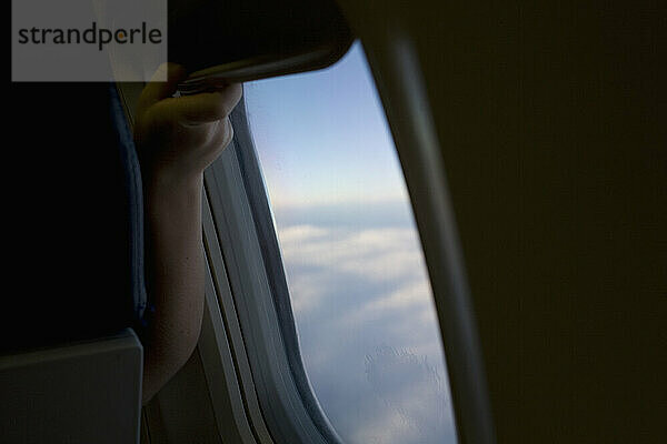 Young traveler adjusts window shade on airliner.