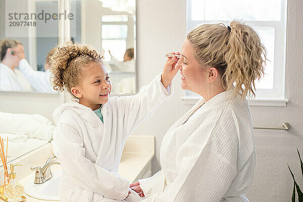 Little daughter is brushing make up on to mothers face in the bathroom