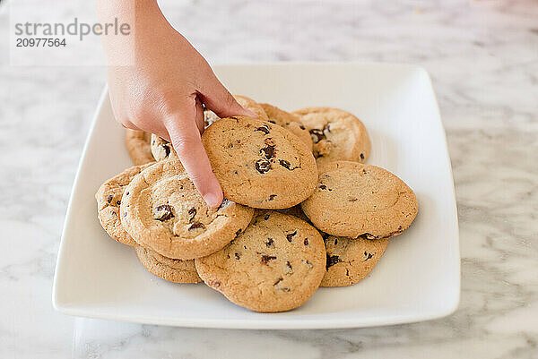 Close up of a little girls hands grabbing a chocolate chip cookie