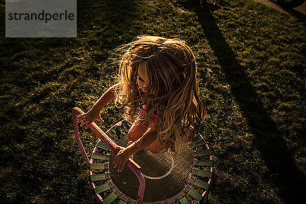 Young girl jumping on trampoline in warm sunlight