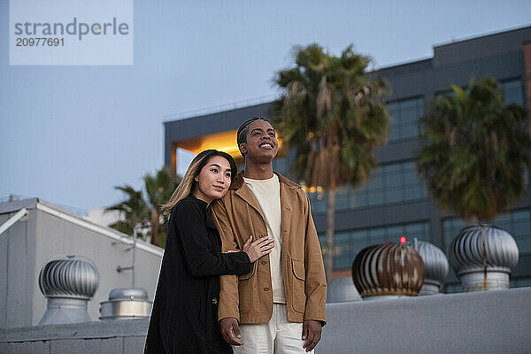 Asian woman embraces black african american male an urban roof-t