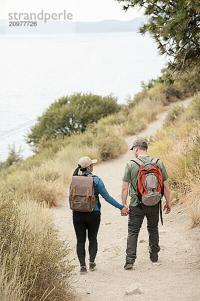 Hiker couple holding hands walking down a trail with backpacks