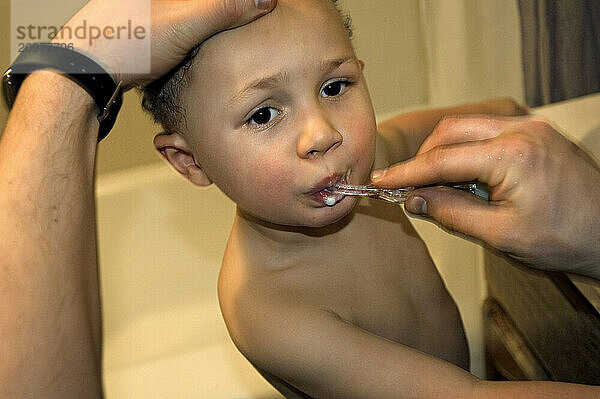 A boy is getting his teeth brushed by his father