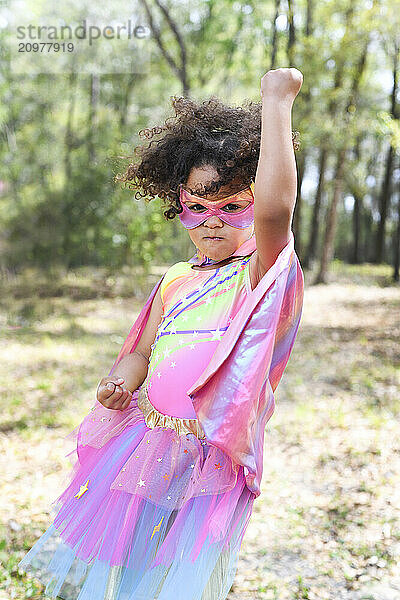 Young girl in superhero costume striking a powerful pose in a fo