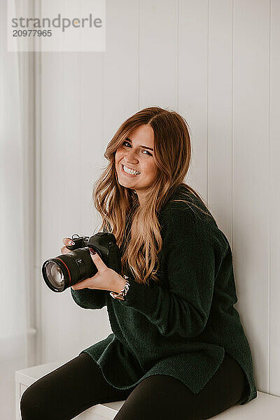 Smiling woman holding a camera  sitting in a bright room