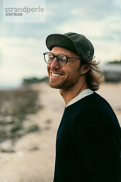 Portrait of smiling man standing at beach against cloudy sky.