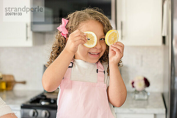 Little girl holding up two lemon slices over her eyes