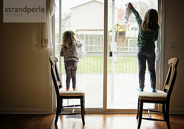 Young sisters washing windows doing chores inside home