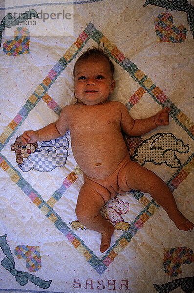 Naked infant laying on blanket in Maine.