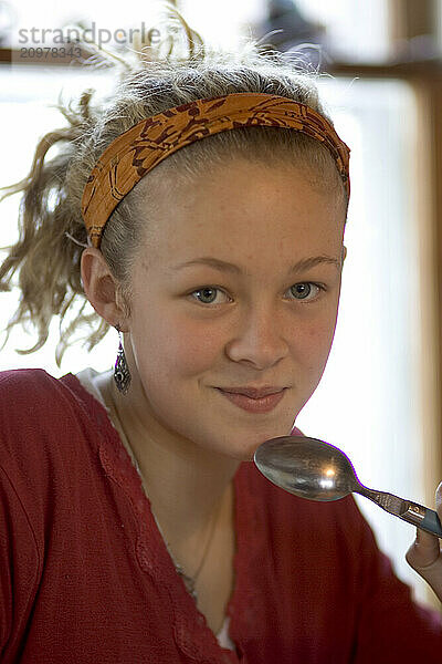 A teenage girl holding a spoon and smiling  Maine  USA.