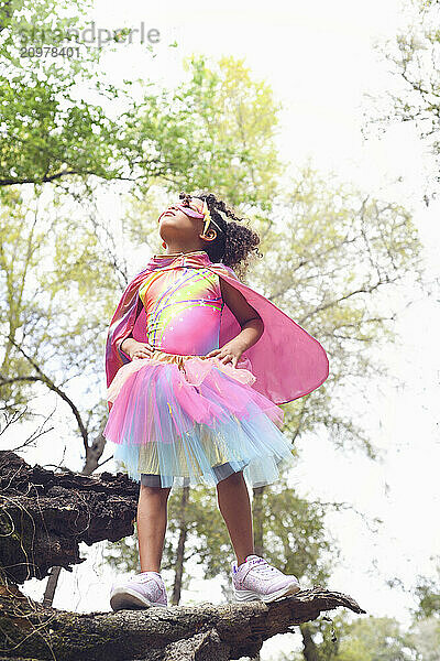 Young girl in superhero costume standing proudly on a log  looki