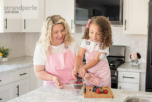 Little girl putting berries in a bowl with mothers help in the kitchen