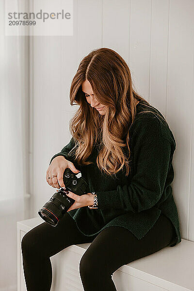 Smiling woman holding a camera  sitting on a white cabinet