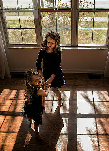 Beautiful young sisters dancing indoors in front of big sunny window