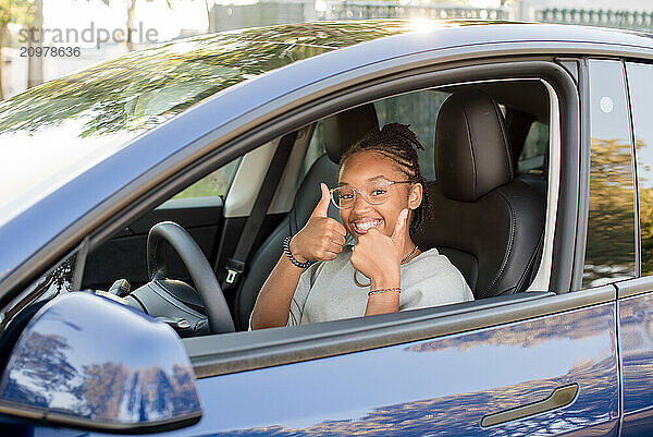 Young adult behind the steering wheel with two thumbs up