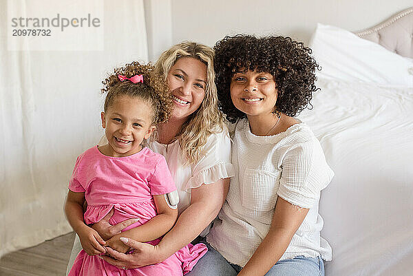 Mother and daughters smiling at camera together in bedroom