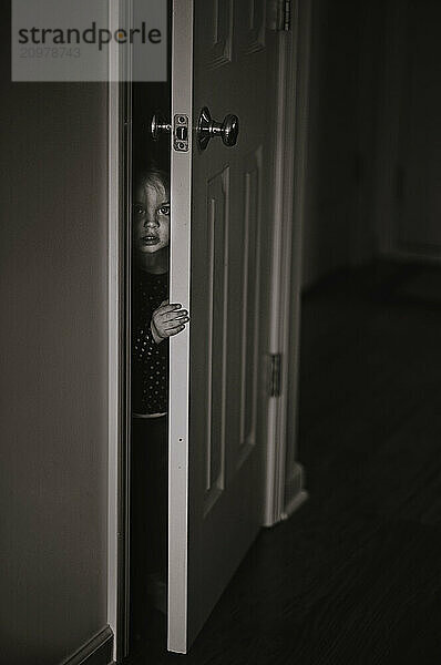 Beautiful toddler peeking through close doors in home