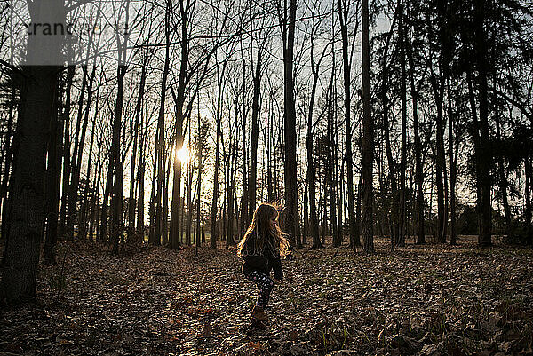 Young girl walking alone through forest at sunset