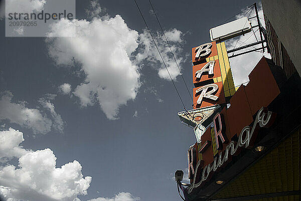 A vintage Bar and Lounge sign hangs in the clouds over Colfax Ave. in Denver  Colorado.