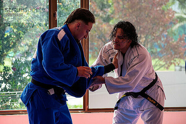 Judo fighters fighting in dojo with big windows at background