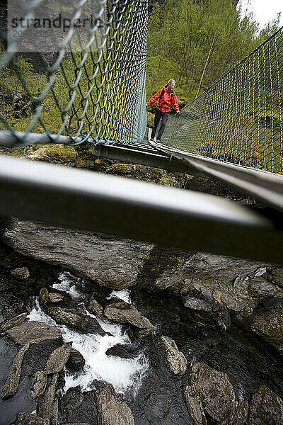 A man crossing a suspension bridge while hiking the Aurland Valley from Osterbo to Vassbygdi in Norway.