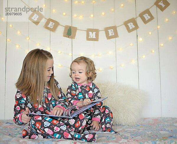 Young sisters reading book in holiday pajamas Christmas backdrop