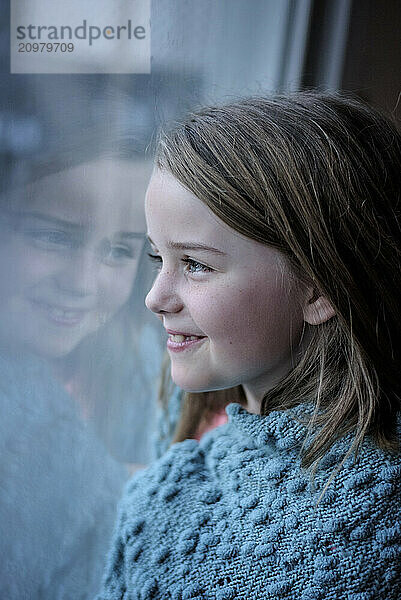 Happy young girl smiling at reflection in window