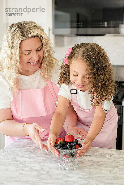 Little girl picking up bowl of berries with mothers help in kitchen