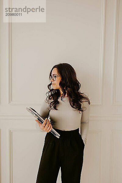 Hispanic woman with notebooks and laptop in hand  white paneled wall