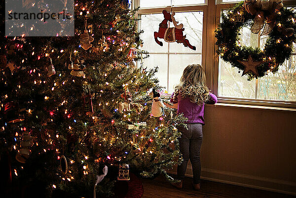 Toddler looking out window next to colorful Christmas tree