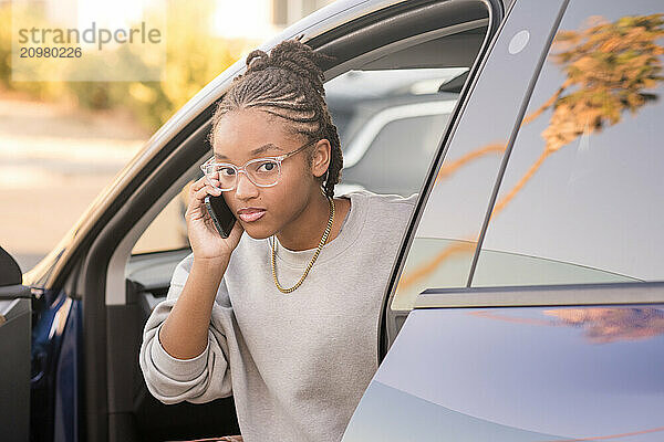 Young lady looking at camera in car while on phone