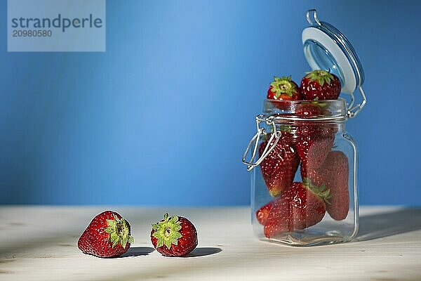 Strawberries on a table and a glass jar full of strawberries with blue background