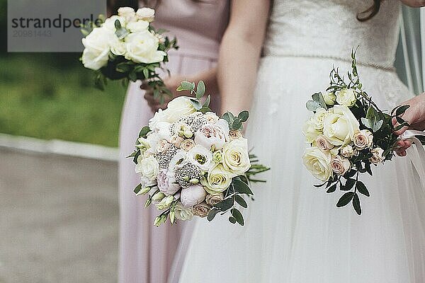 Bride in white dress is holding wedding bouquet with bridesmaids. Blurred background.