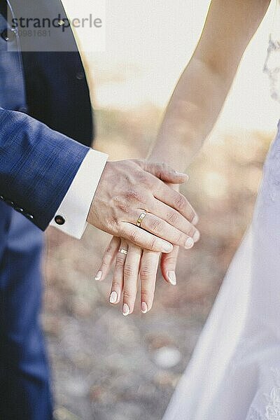 Groom holds bride hand in white dress. Blurred background.