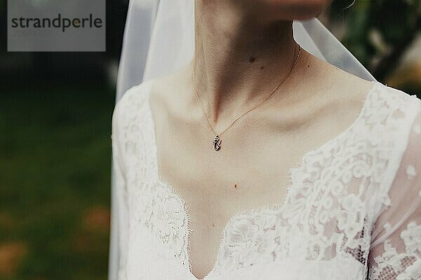 Gold pendant around the neck of the bride in a white dress with veil. Blurred background.