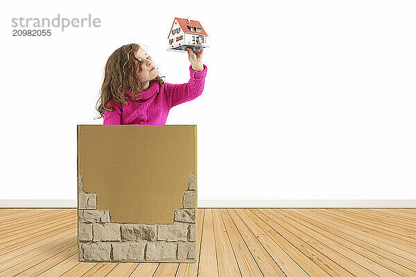 Child sitting in a box looking at a model house