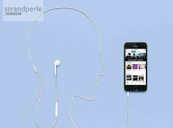 Man head outline made by a headphones cord plugged into iPhone 5s phone with iTunes music store on its display. Creative concept on blue background