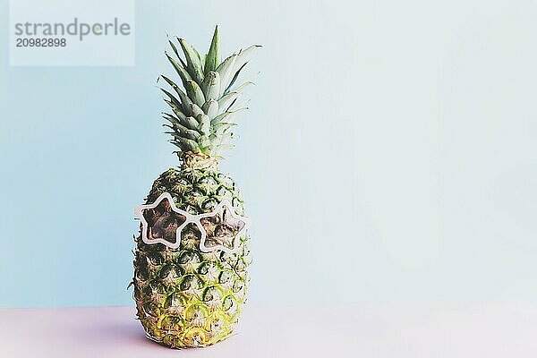 Travel and vacation concept with pineapple wearing sunglasses. Pink glasses in form of star. Relaxation on the sea. Pink and blue background