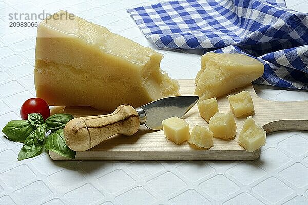 A piece of Parmesan cheese and chopped pieces of cheese on a wooden board