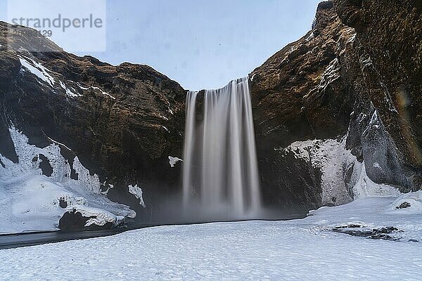 Long exposure of frozen Skogafoss waterfall covered in snow in winter in Iceland