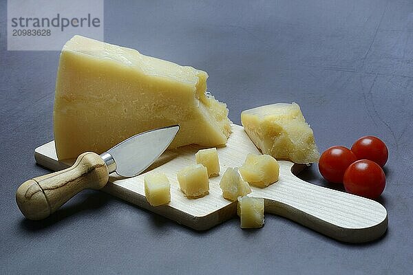 A piece of Parmesan cheese and chopped pieces of cheese on a wooden board