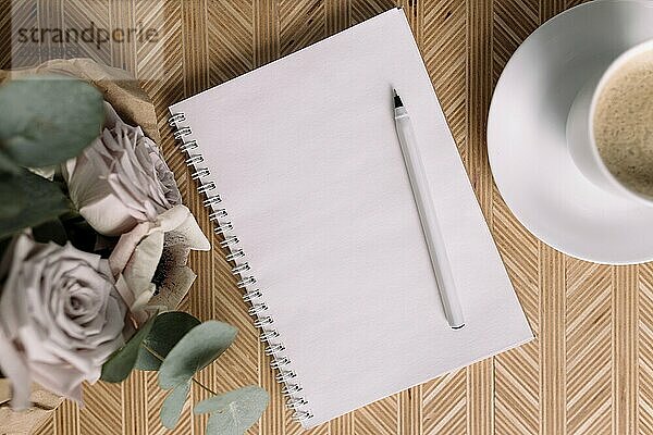 Romantic morning. Wooden coffee table with flowers on bed flat lay  coffee cup  flowers  note pad  pen. Lilac roses with eucalyptus and anemones.