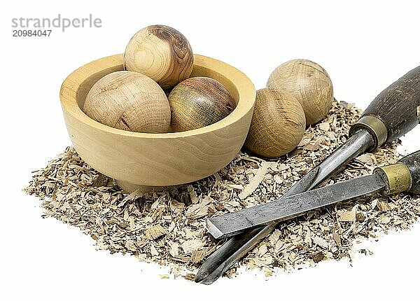 Hand-turned wooden baubles in a bowl decorated with sawdust and tools on a white background