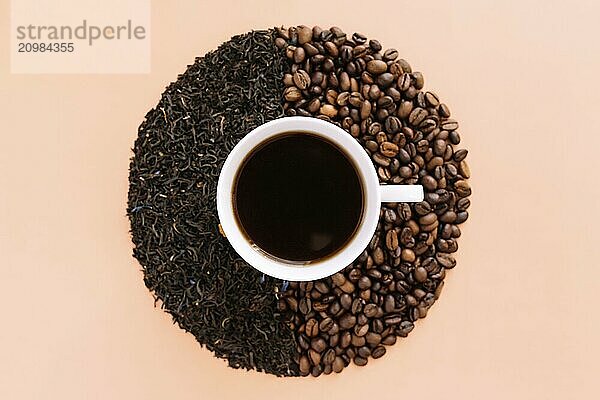 Beige flat lay background with white ceramic coffee cup  roasted coffee beans and dried tea leaves. Idea and composition  choice between coffee beans and dried tea leaves. What is better