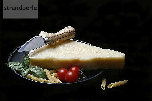 A piece of Parmesan cheese with cheese knife  pasta and tomatoes  Italy  Europe