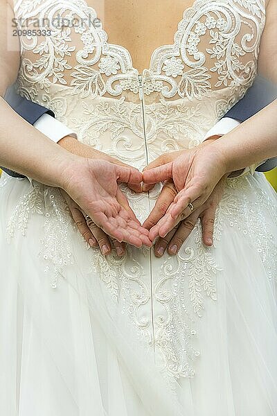 Four hands form a heart on the back of a white wedding dress