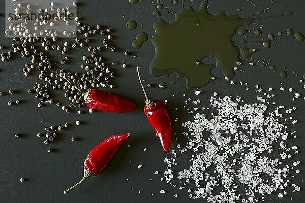 Chili peppers  oil  salt and pepper over a dark background seen from above