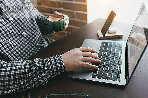 Man working at the laptop with a cup of coffee at home. Blurred background.