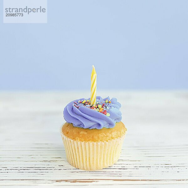 Birthday greetings concept. Yellow candle on a muffin or cupcake. Blue background. Wooden table