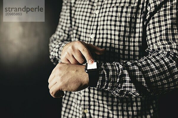 Man in casual clothes clicks hand watches  bracelet  black blurred background.